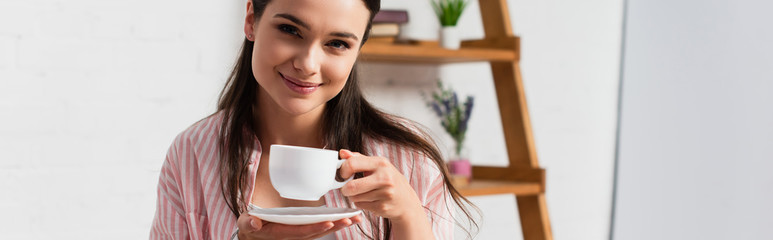 horizontal image of woman looking at camera while holding cup of coffee