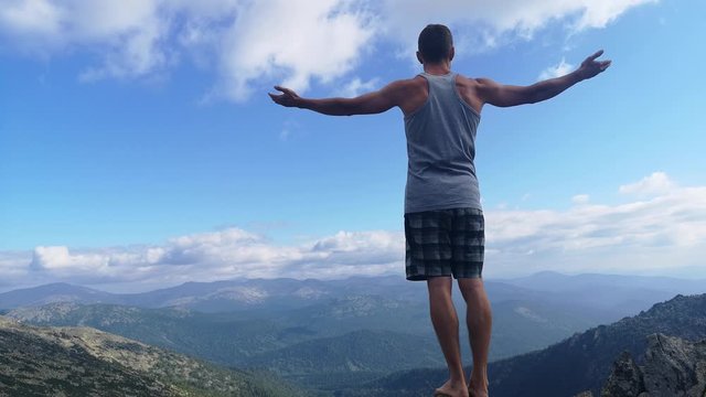 man stands on top of a mountain with open hands. at the top of the mountain, a man with his arms spread wide.