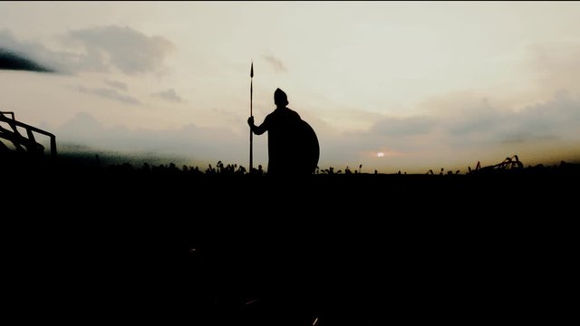 Silhouette of warrior posing with spear in dry field.