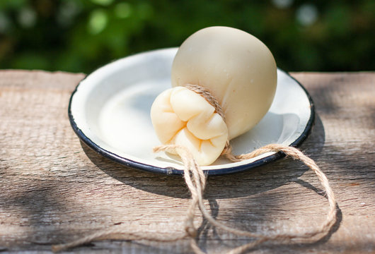 italian scamorza cheese in rustic style in white plate on the old wooden table in the garden