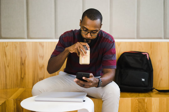 Man drinking iced coffee and looking at smart phone