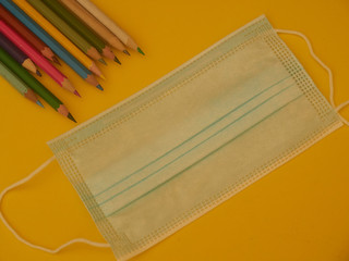 back to school with colored pencils on yellow background and coronavirus mask