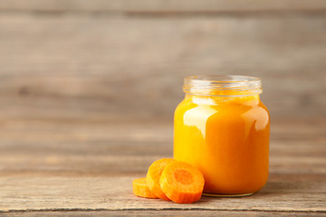 Jar of baby puree with carrot on grey wooden background. Vegetable puree