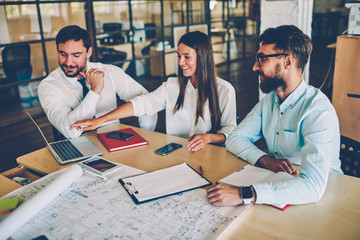 Crew of skilled architects checking accountings in report on laptop computer discussing...