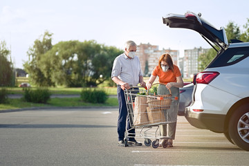Senior couple with face masks putting shopping in car outside supermarket       