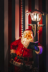 Santa reading book by street lamp in front of  striped wall with lights Stylized