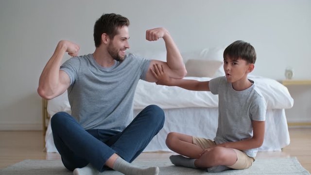 Family fitness at home, Father coach, Sports kid, Fun gymnastics. Son touches dad's bicep and admires looking at the camera