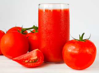 Glass of fresh cold tomato juice and ripe tomatoes on a white background. Close-up.