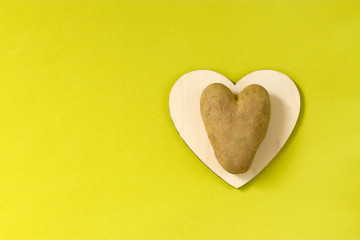 Obraz premium Ugly potatoes in the shape of a heart on a wooden board on a green background. Unusual concept of vegetables. horizontal orientation. Top view. Copy space.
