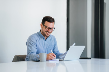 Portrait of a cheerful man having video call on laptop computer cheerful businessman using laptop in bright office space young smiling entrepreneur working writing from home online conference