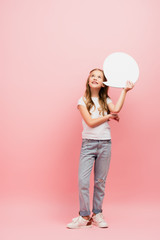 full length view of kid in white t-shirt and blue jeans looking up while holding thought bubble on pink
