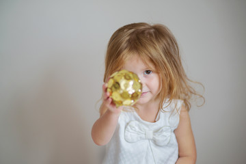 Redhair girl with gold christmas ornament on light gray background 