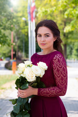 Fototapeta premium girl in a beautiful long burgundy dress with a white bouquet of roses