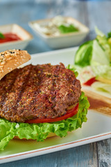 Delicious grilled  burger on white plate on wooden table.  with sauces, french fries and salads.