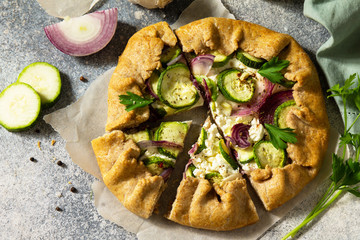 Healthy pastries made from rye flour, dessert diet food. Galette with zucchini, onions and feta on a light stone table.