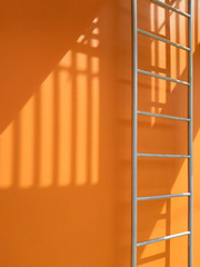 Sunlight and shadow of balusters on surface of fire escape outside of orange building in vertical frame