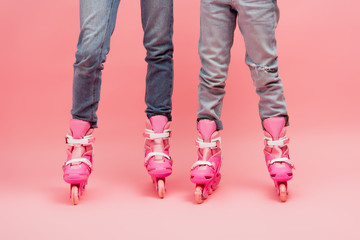 partial view of mother and kid in jeans and roller skates on pink
