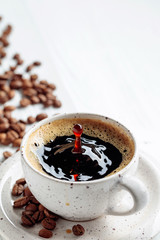 Black coffee and coffee beans on a white wooden table.