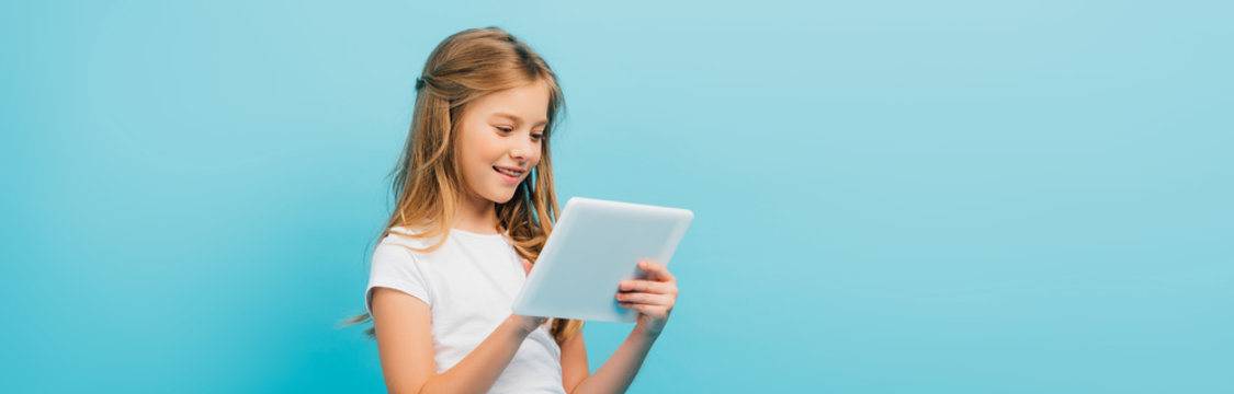 horizontal image of kid in white t-shirt using digital tablet isolated on blue