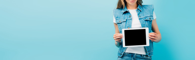 cropped view of woman in denim vest showing digital tablet with blank screen isolated on blue, panoramic concept