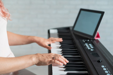 A woman watches video lessons on a digital tablet and plays on an electro synthesizer. The girl...