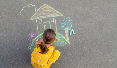 The child draws a house on the asphalt. Selective focus.