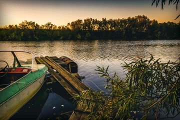 Tranquil evening landscape on the river with an old wooden plank dock and a fishing boat