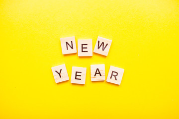 The inscription new year made of wooden blocks on a light yellow background.