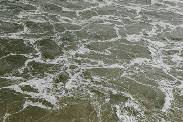 Cold, fresh sea water with foam, deep blue and green water. Closeup view from above for background.