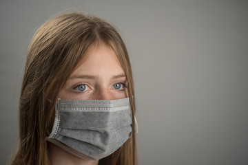 Studio portrait of young girl wearing a face mask, close up, on gray background. Copy space