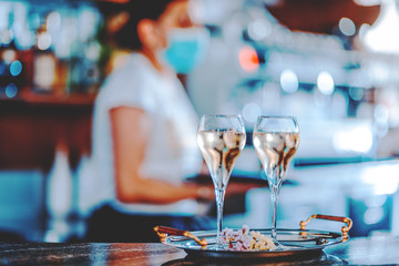 female wine bar tender wearing face mask on the background and two glasses of white sweet wine