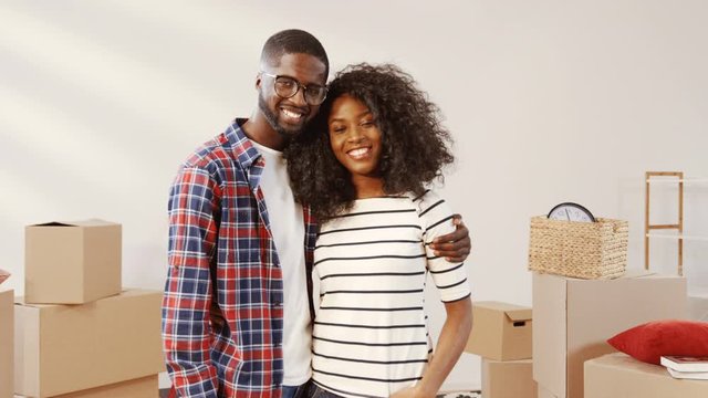 Close up portrait of happy couple in new apartment. Young people hugging among packed boxes. New apartment owners. Moving concept.