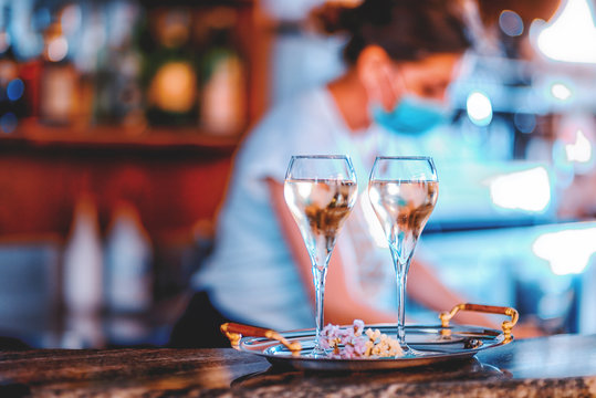 Female Wine Bar Tender Wearing Face Mask On The Background And Two Glasses Of White Sweet Wine