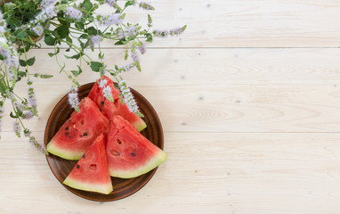 Four slices of ripe watermelon on a plate and a bouquet of blooming oregano. Whitewashed wooden table. The view from the top