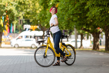 young woman with pink hair walks in the park with a bike eating ice cream in the summer. Environmental mode of transport