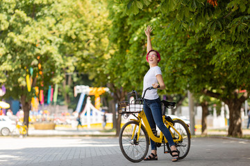 young woman with pink hair walks in the park with a bike eating ice cream in the summer. Environmental mode of transport