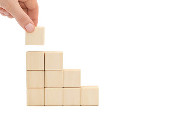 Stairs made of wooden blocks, hand lays down the last cube.