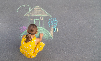 The child draws a house on the asphalt. Selective focus.