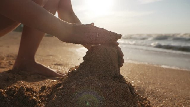 Attractive young woman building sand castle on the beach at sunset