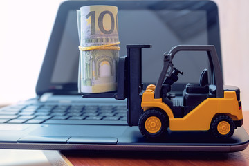Mini forklift truck load stack of banknotes on laptop keyboard. Logistics, transportation,...