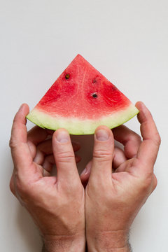 Male hahds holding slice of ripe watermelon on white background, top view