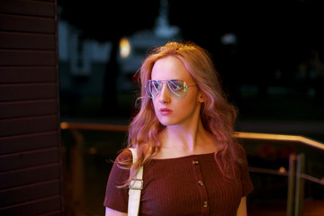 Stylish blonde woman in trendy apparel and eyewear enjoying nightlife in city.