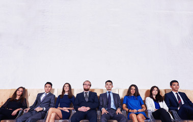 Portrait of a multi ethnic group of a confident business people in corporete clothes sitting in waiting room against wall background with copy space for your text message or promotion content