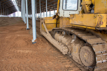 A bulldozer is leveling the ground in a barn under construction. Construction of an agricultural complex. Earthworks using special equipment. Bulldozer is pushing soil in a worksite