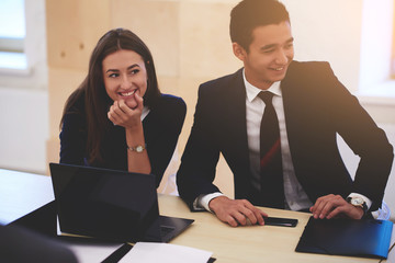 Man and woman with smiles on faces are sitting together in business school at the table with laptop computer and folder with documents. Cheerful two students are taking break between work on net-book