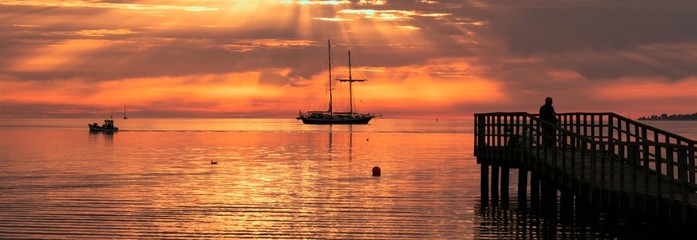 magische Sonnenstrahlen am Steg an der Ostsee mit Segelschiff und Fischerboot