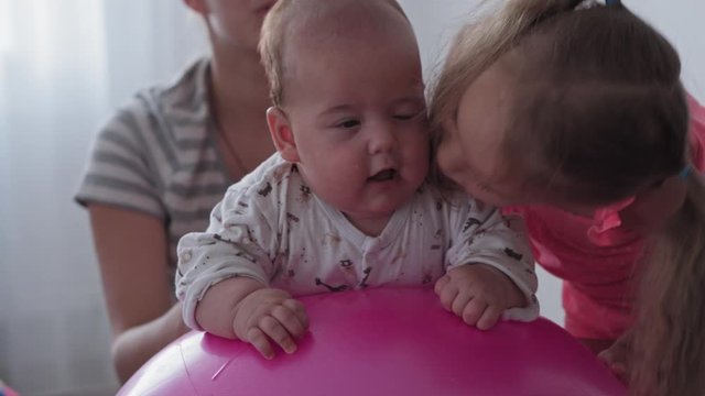 Childhood, Motherhood, games, upbringing and development concept - close-up young mom are joyfully doing exercise and masah with two newborn and little daughters on fitball and smiling in kid playroom
