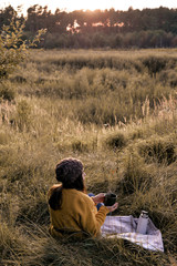 Young girl siiting with cup of tea coffee in yellow  pullover outdoor in picnic in sunset