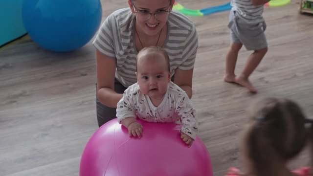 Childhood, Motherhood, games, upbringing and development concept - close-up young mom are joyfully doing exercise and masah with two newborn and little daughters on fitball and smiling in kid playroom