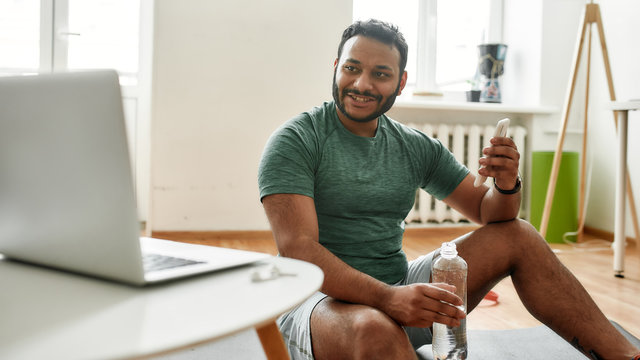 Sharing advice. Young active man smiling, advertising smartphone app while streaming, broadcasting video lesson on training at home using laptop. Online personal trainer - Powered by Adobe